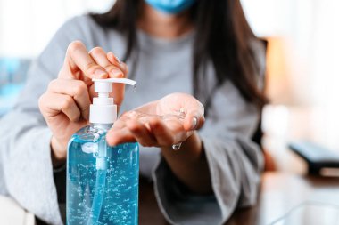 Evden çalışıyorum. Dezenfektan jeliyle ellerini temizliyor. İş kadını koruyucu maske takarak evde çalışıyor..  