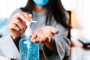 Evden çalışıyorum. Dezenfektan jeliyle ellerini temizliyor. İş kadını koruyucu maske takarak evde çalışıyor..  