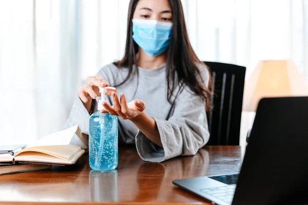 Working from home. Cleaning hands with sanitizer gel. Business woman working from home wearing protective mask.