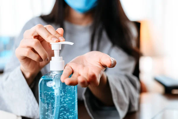 Working from home. Cleaning hands with sanitizer gel. Business woman working from home wearing protective mask.