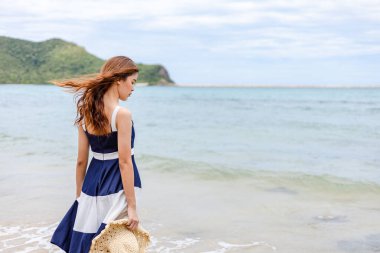 Mutlu genç kız şapkasını tutar ve sahilde yürür. Yaz seyahati, meslek, tatil konsepti.