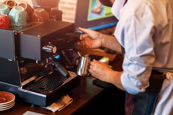 Barista steaming milk in the pitcher with coffee machine for  preparing to make latte art.