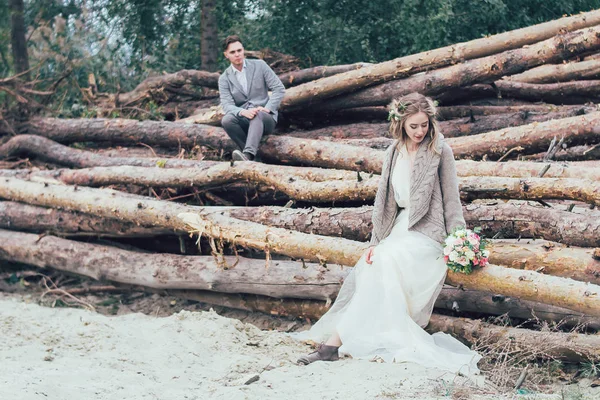 Eine Braut sitzt auf den Baumstämmen mit dem Hochzeitsstrauß — Stockfoto