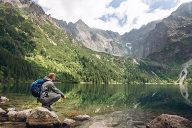 Bir dağ Gölü kıyısında bir taş üzerinde oturan adam bir landcsape sahiptir