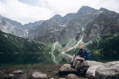 Kayanın üzerinde bir dağ Gölü kıyısında oturan adam