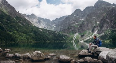 Kayanın üzerinde bir dağ Gölü kıyısında oturan adam bir manzara sahiptir