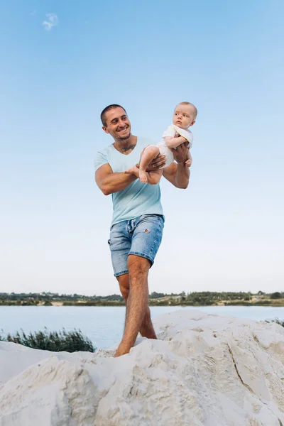 Счастливый отец держит на руках своего маленького сына на песчаном пляже озера — стоковое фото