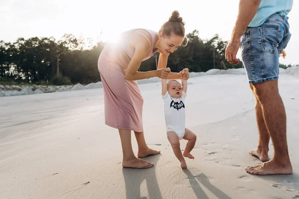 Улыбающаяся мать воспитывает своего маленького сына на песчаном пляже на закате — стоковое фото