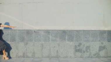 Bayan bina duvarının yanında yürüyor. Gri tuğlalara dokunuyor.