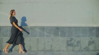 Yüksek topuklu ayakkabılı profesyonel model gri duvarın yanından geçiyor.