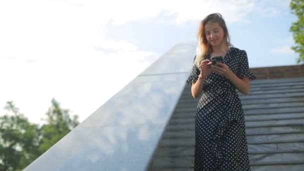 Sonriente dama en vestido va abajo grandes escaleras leyendo sms — Vídeo de stock