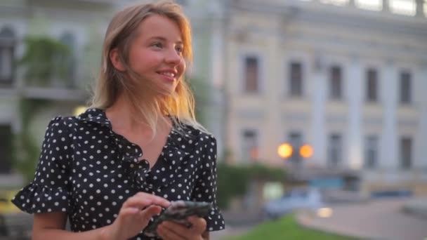 Tyttö pitkät löysät hiukset kävelee pitkin kaupungin keskustaa auringonlaskun aikaan — kuvapankkivideo