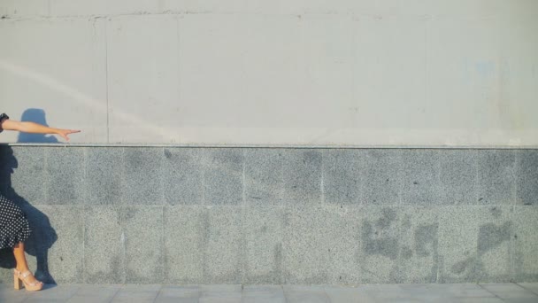 Женщина идет рядом со стеной здания касаясь серых кирпичей верхней линии — стоковое видео