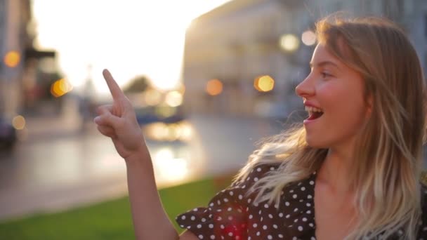 Chica levanta dedo índice y sonríe contra ciudad borrosa — Vídeos de Stock