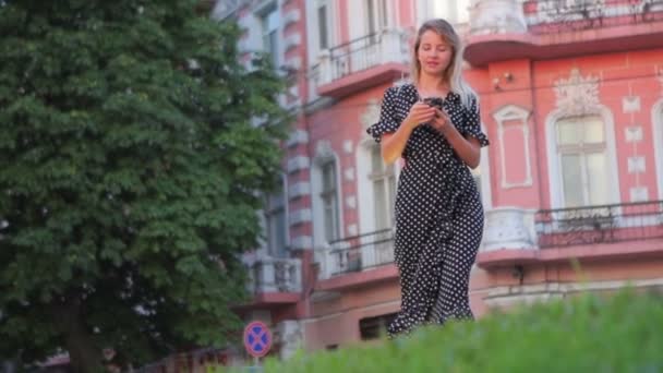 Modèle promenades le long de la route de la ville avec smartphone dans les mains — Video