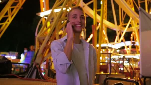 Mann steht mit Handy in Vergnügungspark neben Riesenrad — Stockvideo
