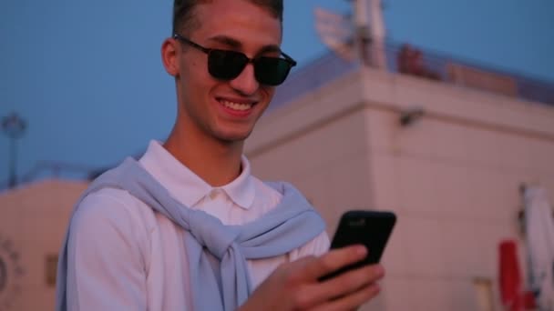 Stylish guy chats on smartphone and looks at city buildings — Stock Video