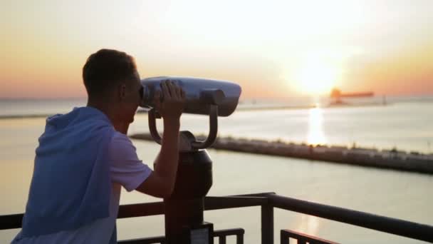 Hombre mira en prismáticos viendo el paisaje marino al atardecer rojo — Vídeo de stock