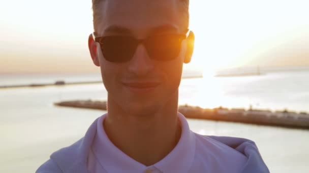 Trevlig kille poserar mot solnedgången ovanför gränslöst lugnt hav — Stockvideo