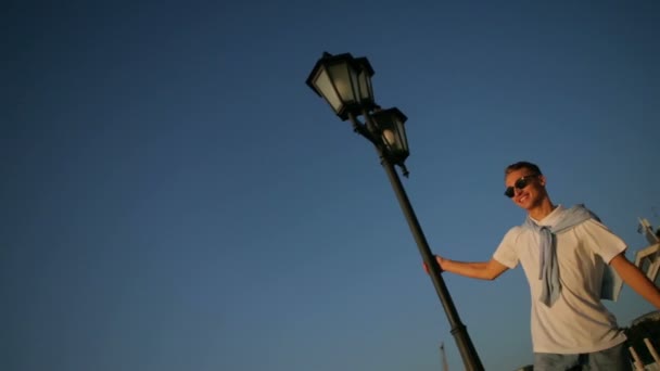 Chlap se otáčí kolem lampy tyč těší západ slunce na promenádě — Stock video