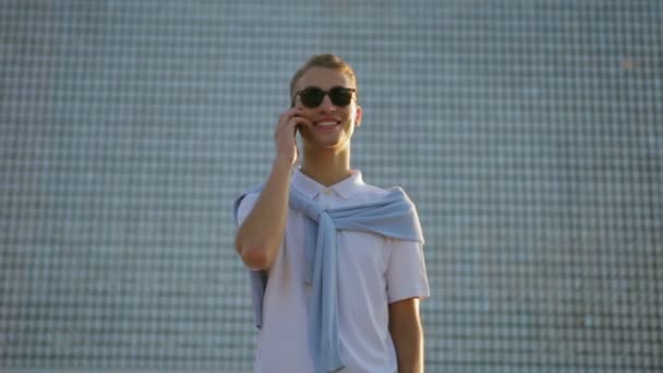 Hombre con estilo responde a la llamada telefónica posando en la pared del rascacielos — Vídeos de Stock