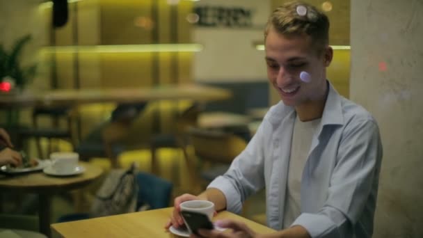 Хлопець п'є каву і текстові повідомлення, сидячи в кафе — стокове відео