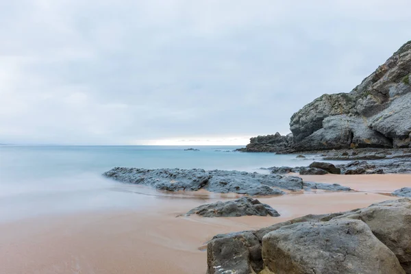 Una foto a lunga esposizione di una spiaggia con rocce in primo piano — Foto Stock