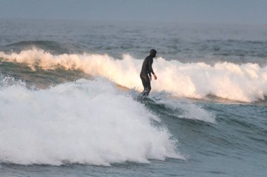 Dalganın tepesinde kameraya arkası dönük tanınmaz bir sörfçü.