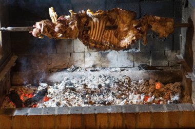 Yanan kömürü çevreleyen demir bir kılıca yerleştirilmiş yarım kuzu barbeküsü.