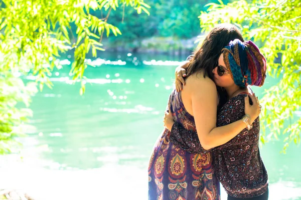 Woman hugging another woman with cancer on a beautiful riverbank.