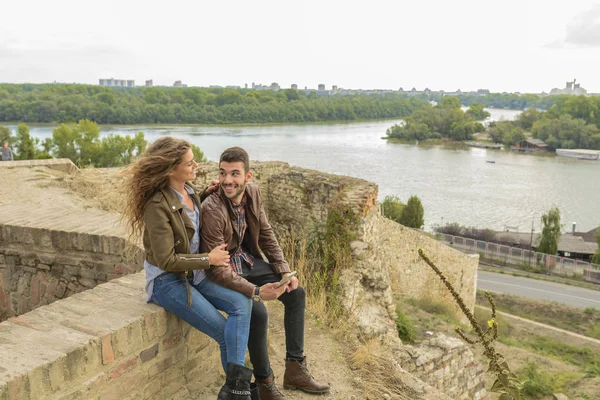 Casal jovem moderno usando seu telefone celular perto do rio — Fotografia de Stock