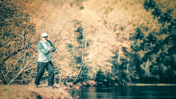 Fischer mit einer Spinnrute, die Fische auf einem Fluss fängt — Stockfoto