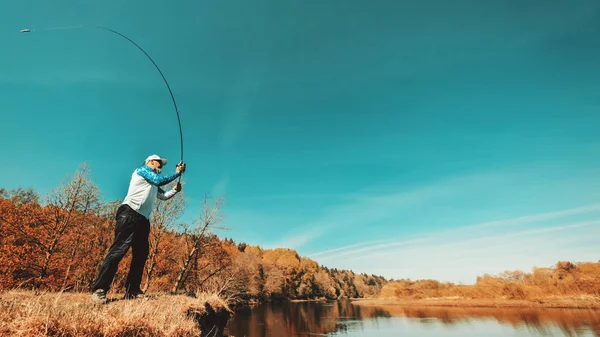 Pescatore con una canna da spinning cattura pesce su un fiume — Foto Stock