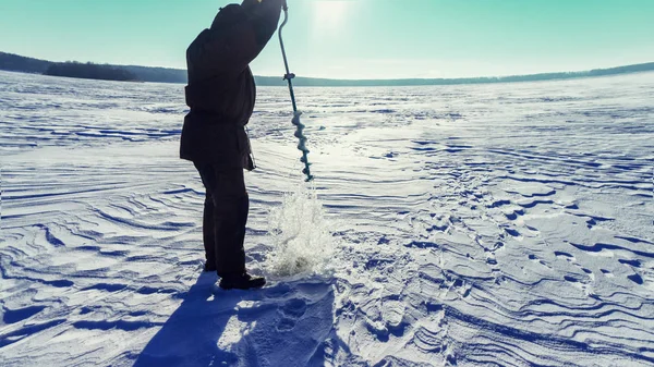Ο ψαράς τρυπάει τον πάγο. Χειμερινή αλιεία. — Φωτογραφία Αρχείου
