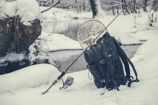 Род, рюкзак и посадочная сетка на берегу зимней реки. Рыболовные снасти . — стоковое фото