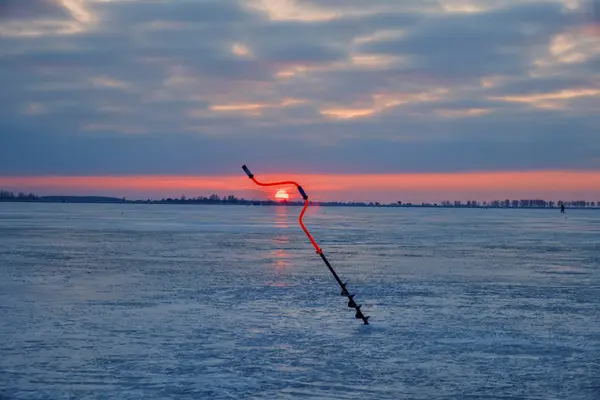 Рыбалка на льду. Бур на фоне восходящего солнца . — стоковое фото