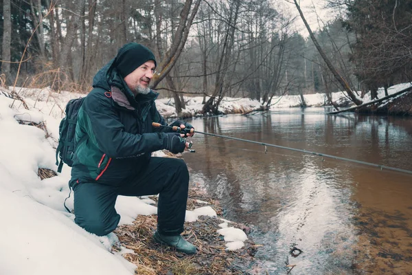Pescatore con una canna sulla riva del fiume. Pesca della trota. Filatura invernale . — Foto Stock