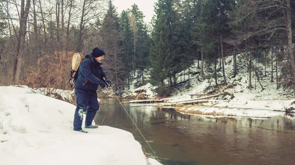 Angler com uma vara na margem do rio. A pescar trutas. Girando inverno . — Fotografia de Stock