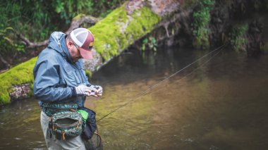 Balıkçı, orman nehrinin arka planındaki yemi değiştiriyor..