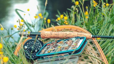 Nehir kıyısında sineklerle uçan olta ve kutu..