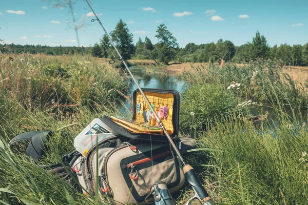 Bolsa con elementos esenciales de pesca en la orilla del río en el día soleado — Foto de Stock