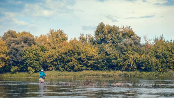 Un pescatore getta una canna da spinning mentre in piedi in un fiume . — Foto Stock