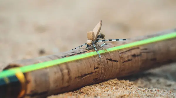 Una hermosa mosca seca se sienta en el mango de una caña de pescar . — Foto de Stock