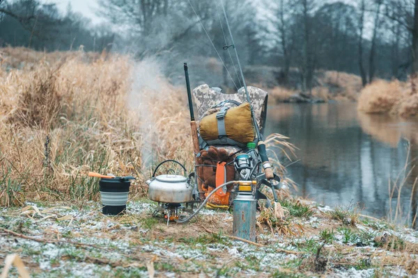 Prepare coffee on a hiking trip. Gas burner and boiling kettle. Fishing equipment in a backpack. — Stock Photo, Image
