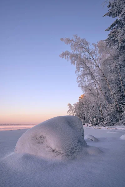 Les pierres sont recouvertes de neige sur le rivage d'un lac forestier d'hiver . — Photo