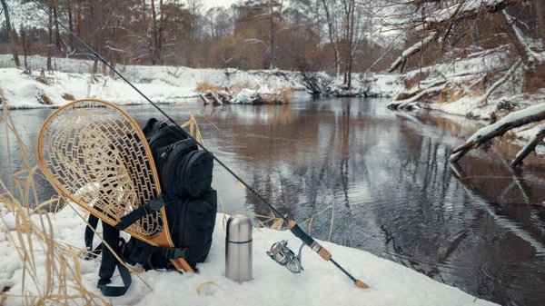 Rugzak en vismateriaal aan de oever van de rivier de winter. — Stockfoto