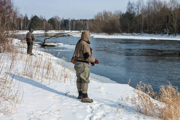 Pescatore pesca su un fiume invernale innevato . — Foto Stock