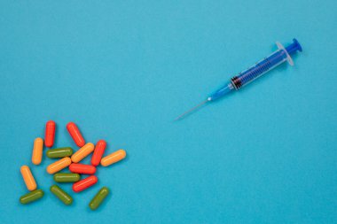 Masaya, şırıngaya ve şırıngaya çok renkli haplar saçılmış. Kopyalama alanı olan üst görünüm, düz yatay.