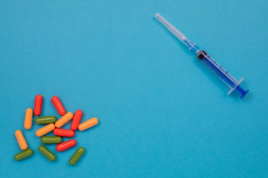 Masaya, şırıngaya ve şırıngaya çok renkli haplar saçılmış. Kopyalama alanı olan üst görünüm, düz yatay.