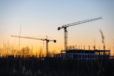 Endüstriyel vinç ve bina siluetleri gün batımında ya da şafakta bir inşaat sahasında.